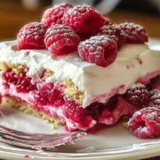 A creamy No-Bake Raspberry Split Cake with a golden graham cracker crust, smooth cheesecake filling, and a vibrant raspberry topping, garnished with fresh raspberries and mint leaves.